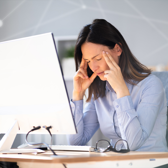 A woman rubbing her temples next to a computer after a breach